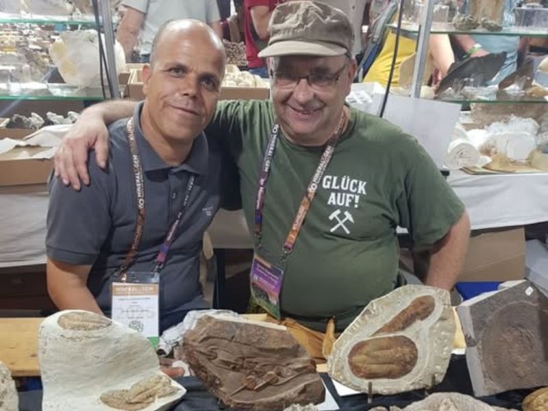 Moi avec un ami d’Erfoud sur son stand de minéraux lors du salon minéralier de Sainte-Marie-aux-Mines, avec pierres naturelles exposées.
