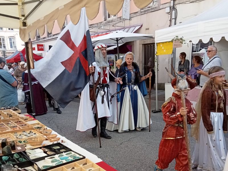 Vue depuis le stand TerraCristaux montrant le passage d’une parade de Templiers, avec public et animations médiévales.